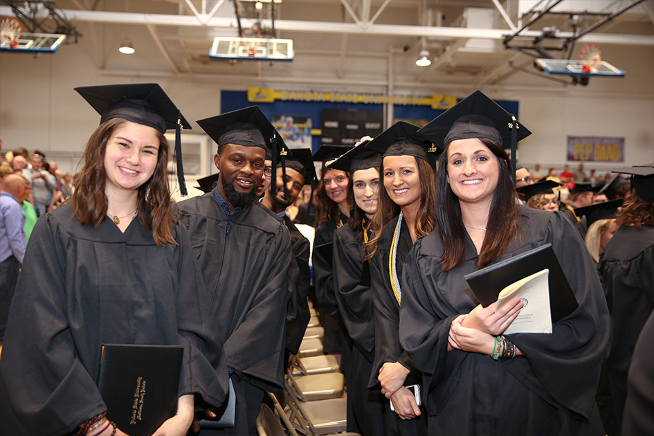 students in graduation gowns holding diplomas