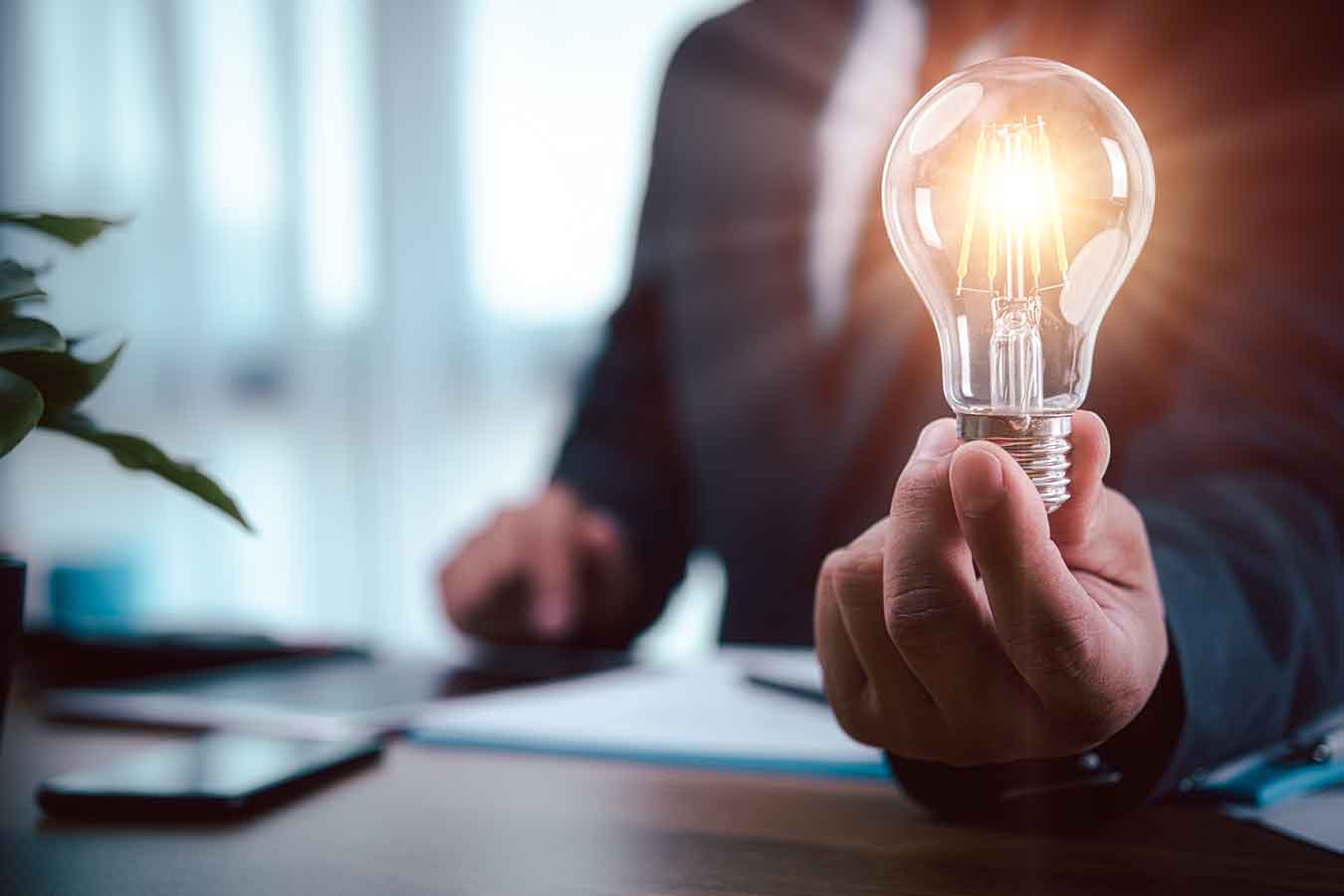 lit lightbulb held in a hand atop a desk.